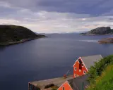 Widok na fiord, czerwone domy rybackie i góry w tle. Prom Bodo Moskenes czeka na podróżnych.