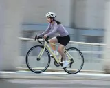 Uśmiechnięta kobieta w kasku pędzi na rowerze, ciesząc się sportami rowerowymi.