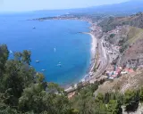 Widok na wybrzeże Sycylii, gdzie najcieplej w kwietniu. Błękitne morze, plaża, miasteczko i góry.