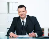 Uśmiechnięty mężczyzna w garniturze pisze w notatniku, przygotowując się do konkursu na dyrektora szkoły.