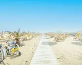 Una passerella bianca conduce alle spiagge di Riccione, con sdraio e ombrelloni pronti per accogliere tutti, compresa una sedia a rotelle speciale per la sabbia.