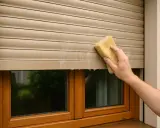 Mycie rolet zewnętrznych gąbką. Woda spływa po lamelach, okno jest czyste.