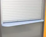 Zasłonięta roleta zewnętrzna z szarą półką. Widoczny fragment przewodu do rolet zewnętrznych.