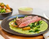 Saftig flankstek ugn serveras med rostade potatisar, grönsaker och en krämig örtsås. En festlig måltid!