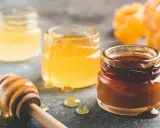 Trois pots de miel aux teintes variées, du clair au foncé, et une cuillère en bois dégoulinante. Quel miel pour pain d'épices ? Le choix est là !