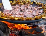 En stor stekpanna över öppen eld där kött och potatis tillagas. En perfekt dag att laga mat ute!