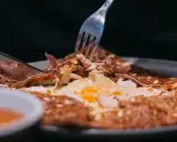 Une galette garnie d'œuf et de poulet, un délice des spécialités de Bretagne, est coupée avec un couteau et une fourchette.