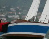 Couple en action sur un voilier transportable, naviguant sur des eaux agitées avec un village en arrière-plan.