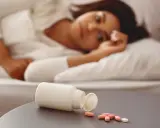 Frau liegt im Bett, daneben eine offene Pillendose mit Tabletten. Vielleicht die Suche nach Schlaf mit Melatonin maximaldosis.
