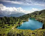 Laghi di San Giuliano: un'oasi alpina con acque turchesi, circondata da fitti boschi di conifere e montagne maestose sotto un cielo azzurro con nuvole bianche.