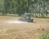 Traktor rozsypuje wapno na polu, pokazując, co daje wapnowanie gleby. Poprawia jej strukturę i żyzność.