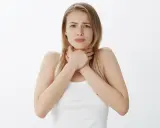 Młoda kobieta zaniepokojona, trzymająca się za gardło, jakby czuła flegmę w gardle po jedzeniu.