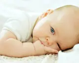 Niemowlę z niebieskimi oczami leży na boku, wkładając rączkę do ust. To uroczy moment, od kiedy niemowlę wkłada rączki do ust, odkrywając świat.