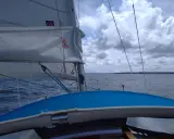 Vue depuis un voilier, le **lofer voile** blanc gonflé par le vent, sur une mer agitée sous un ciel nuageux.