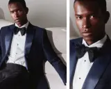 A man in a dark blue dinner jacket vs tuxedo, with a satin lapel and black bow tie, poses on a textured sofa.