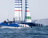 Catamaran bleu et blanc, voiles rayées, en pleine action. La **vitesse catamaran** est impressionnante, les foils hors de l'eau.