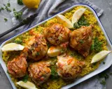 Poulet piri piri savoureux sur un lit de riz jaune, garni de quartiers de citron et de persil frais. Un délice épicé à partager.