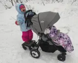 Dziecko na sankach z przodu spacerówki joie litetrax 4, z drugim dzieckiem w środku, na śniegu.