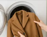 Manos colocando un abrigo de paño marrón en una lavadora.