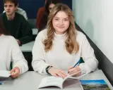 Uśmiechnięta studentka pisze w zeszycie, idealne zdjęcie do legitymacji.