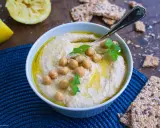 Cremiger Hummus, garniert mit Kichererbsen und Petersilie, daneben Zitronenspalten und knusprige Cracker. Das ist das beste Hummus Rezept!