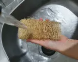 Ein Luffa Schwamm wird unter fließendem Wasser in der Spüle gereinigt.
