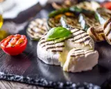 Grillowany camembert z pomidorkiem, cukinią i pieczarkami na czarnej desce.