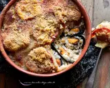Piatto invitante di riso patate e cozze, gratinato con pomodoro e pangrattato, servito in una terrina di terracotta.