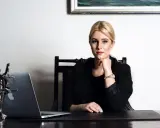 Kobieta w czarnej marynarce siedzi przy biurku z laptopem i figurką Temidy.