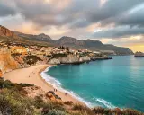 Traumhafte Bucht auf Sardinien im Oktober. Das Wetter ist mild, die Sonne bricht durch die Wolken und taucht die Küste in warmes Licht. Ein perfekter Tag für einen Spaziergang am Strand.