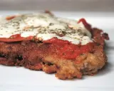 En närbild på en gyllene milanesa napolitana med smält ost, tomatsås och örter.