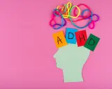 Kolorowe sznurki nad głową symbolizują chaos myśli, jak przy ADHD. Kartki z literami A, D, H, D sugerują trudności w nauce, np. dyskalkulię.