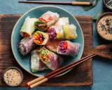 Assiette de rouleaux de printemps colorés, remplis de légumes frais et servis avec une sauce tahini.
