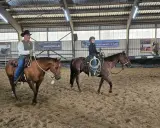 Mann mit Hut und ein Jugendlicher üben Reining Reiten in einer Reithalle.