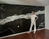 Pintor posa frente a una pared con falso estuco de mármol negro y blanco.