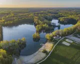 Malownicze jezioro Czechowice otoczone zielonym lasem, z piaszczystą plażą i zabudowaniami rekreacyjnymi.