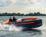 Deux hommes naviguent sur un bateau rapide, créant des éclaboussures. Le design moderne du bateau, avec ses accents orange vif, suggère une conception soignée, peut-être pour fabriquer des flaps pour bateau.