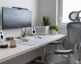 Installation poste de travail épurée avec écran, clavier, souris, enceintes blanches, plantes et chaise ergonomique grise.
