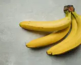 Kilka żółtych bananów leżących na szarym tle.