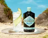 Ein erfrischender Gin Tonic mit Hendricks Neptunia Gin, Gurkenscheiben und Eis, auf sandigem Untergrund mit Felsen und blauem Himmel.