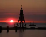 Sonnenuntergang in Cuxhaven: Ein Leuchtfeuer und ein Fischerboot auf dem Meer. Hier kann man die Weite genießen und den Tag ausklingen lassen.