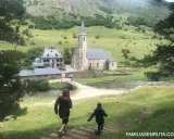 Dos niños corren por un sendero en un valle verde hacia una iglesia y casas de piedra. ¡Un plan perfecto de qué hacer en Vielha con niños!