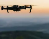 Czarny dron unosi się nad wzgórzami o zachodzie słońca.