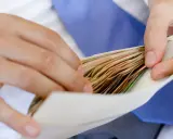 Dłonie wkładają plik banknotów do koperty na wesele.