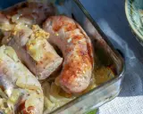 Soczysta biała kiełbasa pieczona z cebulką i musztardą, podana w szklanym naczyniu.
