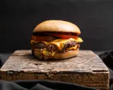 Saftiger Oklahoma Smash Burger mit geschmolzenem Käse und Tomaten auf rustikalem Holzbrett.