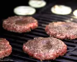 Vier frisch geformte Patties, gewürzt mit Pfeffer, brutzeln auf dem Grill. Perfekt, um Patties selber machen.