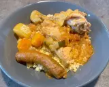 Un plat appétissant de tajine poulet merguez, servi sur un lit de semoule, avec des morceaux de poulet, des légumes et une merguez dorée.