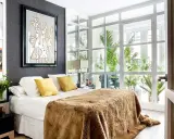Un dormitorio moderno con cama mullida, arte abstracto y ventanales que invitan a diseña tu dormitorio con luz natural y plantas.