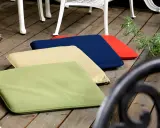 Mehrere bunte gartenpolster nass geworden, liegen auf einer Holzterrasse neben Gartenmöbeln.